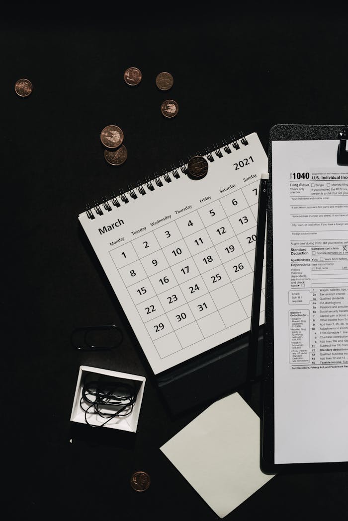 Top-down view of coins, a calendar, and tax form on a dark surface.