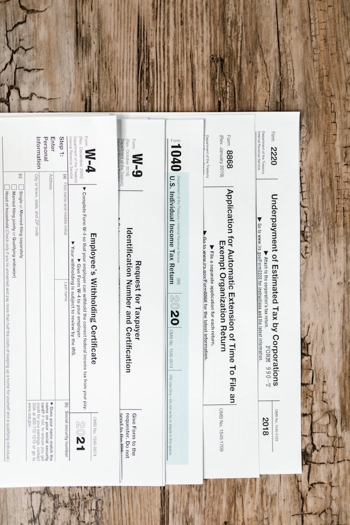Close-up of various U.S. tax forms including W-4, W-9, and 1040 on a rustic wooden surface.